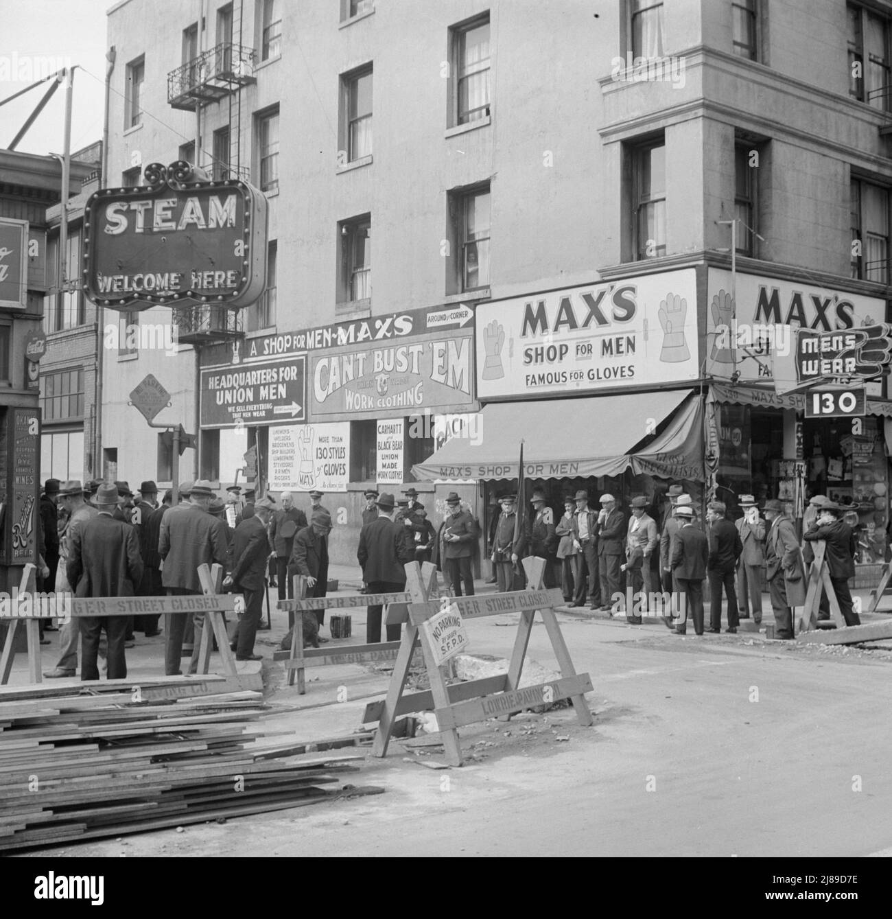 Salvation Army, San Francisco, Kalifornien. Allgemeine Sicht auf Armee und Menschenmengen. [Schilder: „Danger - Street Closed; Steam Welcome here; Headquarters for Union Men - We Sell Everything Men Wear; Can't Bust 'EM Work Clothing; Max's Shop for Men - Famous for Gloves“]. Stockfoto