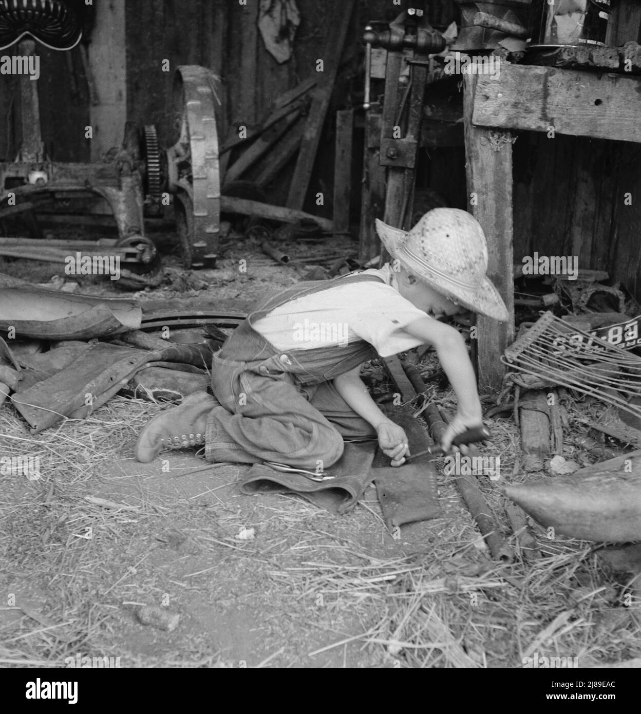 Junger Bauernjunge. Jüngerer Bruder, der versucht, aus dem Leder eines alten Mantels ein Holster zu machen. Oregon, Jackson County, in der Nähe von Medford. Stockfoto