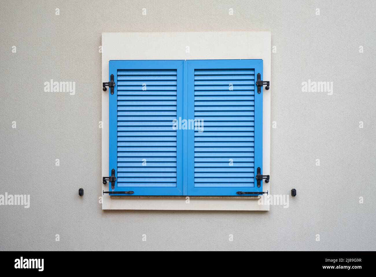 Blaue Kunststoff-Fensterläden an einer Wand des Wohngebäudes Stockfoto