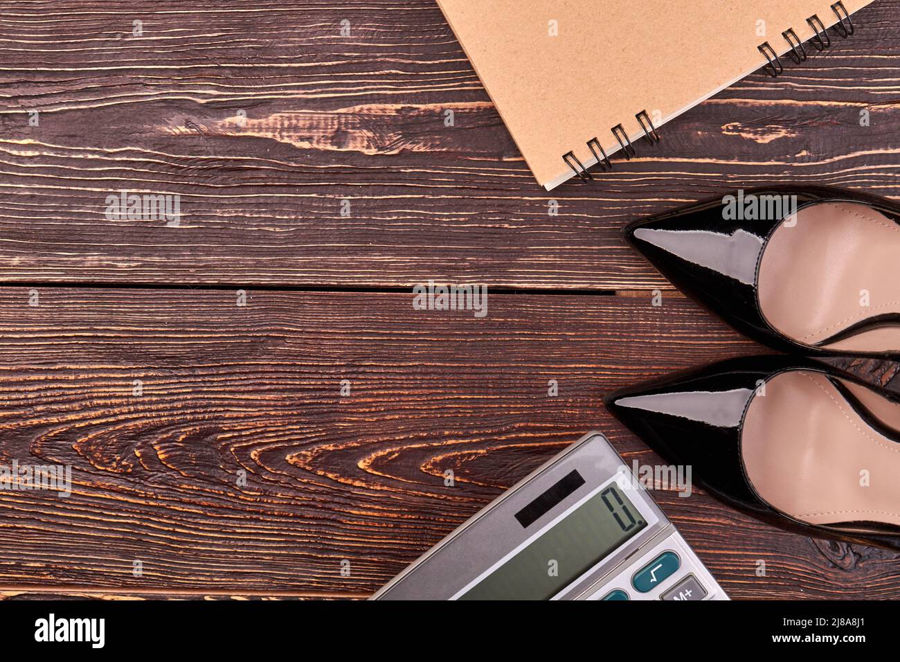 Schuhe mit Taschenrechner und Notizblock auf braunem Holztisch. Draufsicht flach liegend. Stockfoto