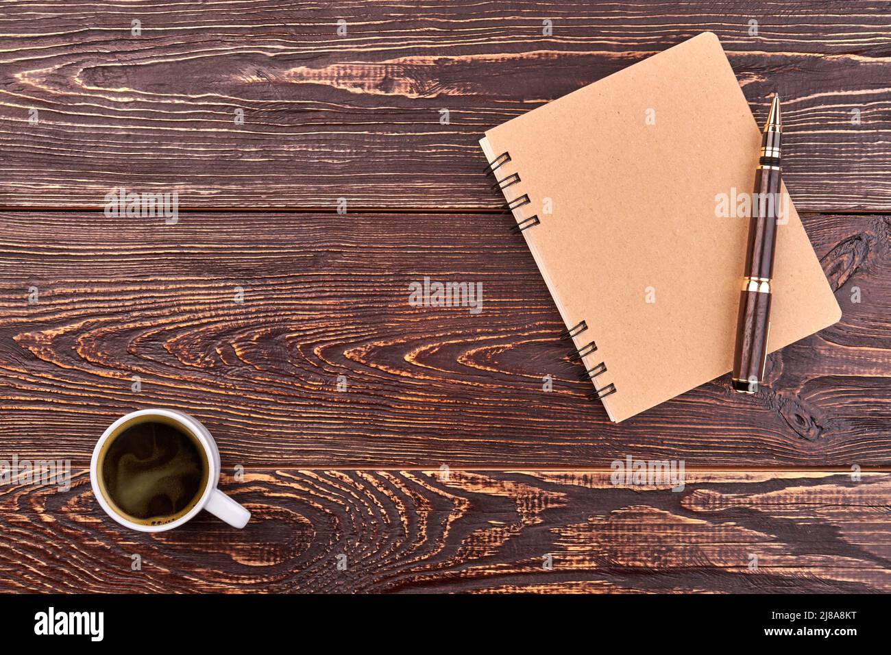 Notizblock mit Stift und Tasse Kaffee. Schreibtisch aus braunem Holz und Platz für Kopien. Stockfoto