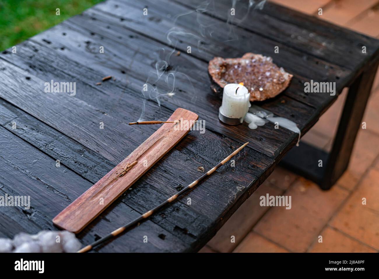 Ein Holztisch im Freien mit Räucherstäbchenhalter, Stab, Kerze und spirituellen Kristallen, die ein kraftvolles Ambiente schaffen Stockfoto