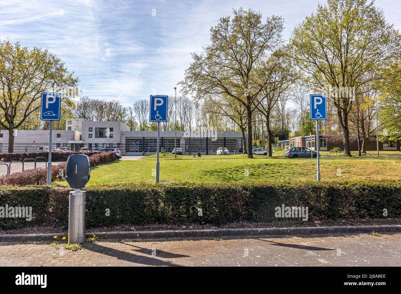 Öffentlicher Parkplatz mit Stellplätzen für Handicap und Ladestation für Elektroautos, blaue Schilder mit einem P, eine Zeichnung eines Rollstuhls und ein Auto mit einem e Stockfoto