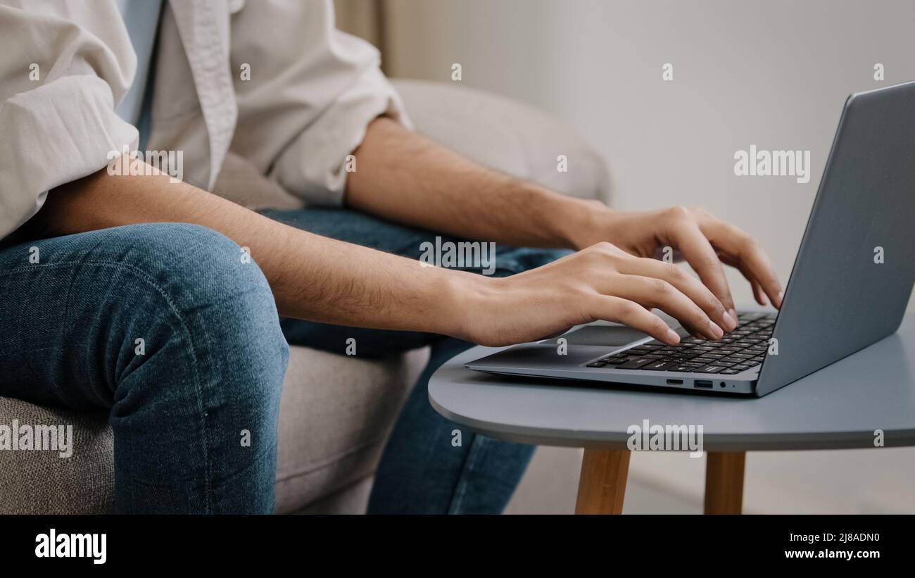 Nahaufnahme der männlichen Hände, die auf der Laptop-Tastatur tippen. Unkenntlich unbekannter Geschäftsmann in Jeans Casual Shirt sitzt auf dem Sofa mit Computer arbeiten Stockfoto