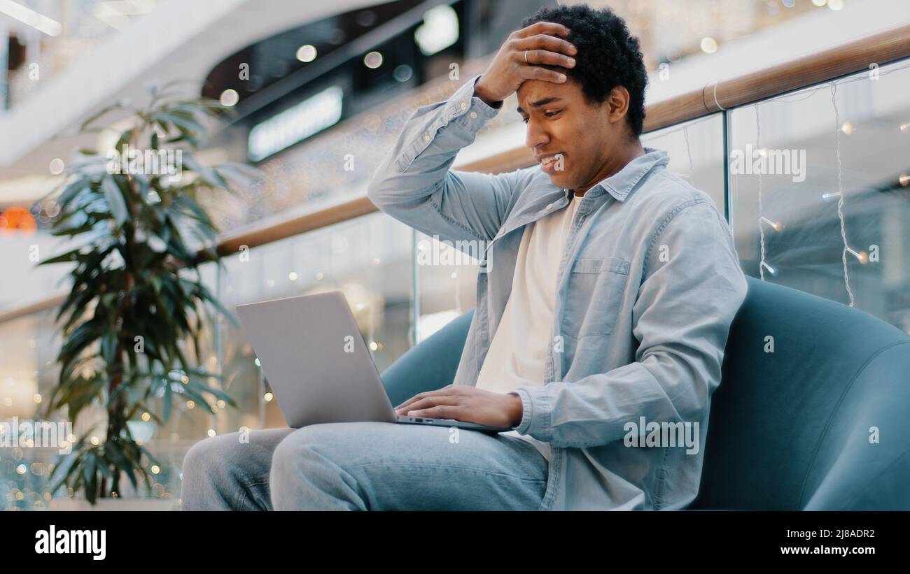 Multirassischer Kerl Freiberufler afrikanischer traurig frustrierter Geschäftsmann mit Laptop sitzt auf der Couch verlieren in Online-Wetten-Spiel Geld im Internet verloren Stockfoto
