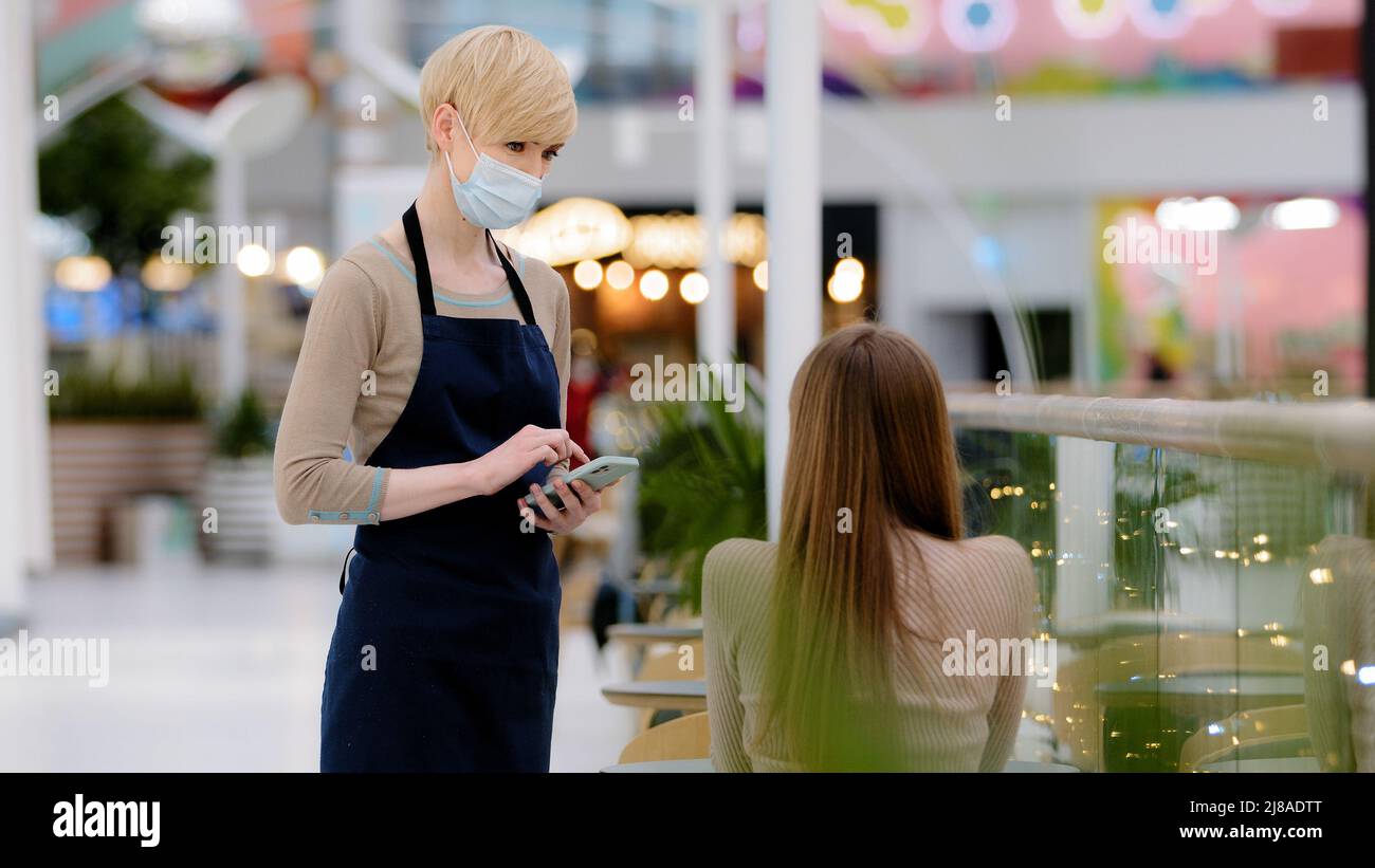 Frau Kellnerin Angestellter Arbeiter der Cafeteria Restaurant im Vorfeld und medizinische Maske dient Gespräche mit weiblichen Kunden Mädchen am Tisch sitzt schreibt Stockfoto