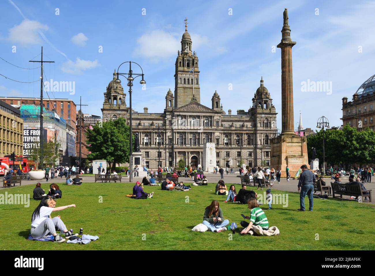 14., Mai 2022. Glasgow, Schottland. Warmer, sonniger Tag in Glasgow nach kalter Wind und Regen unter der Woche. Menschen sitzen auf dem George Square in Glasgow mit den ratskammern im Hintergrund Stockfoto