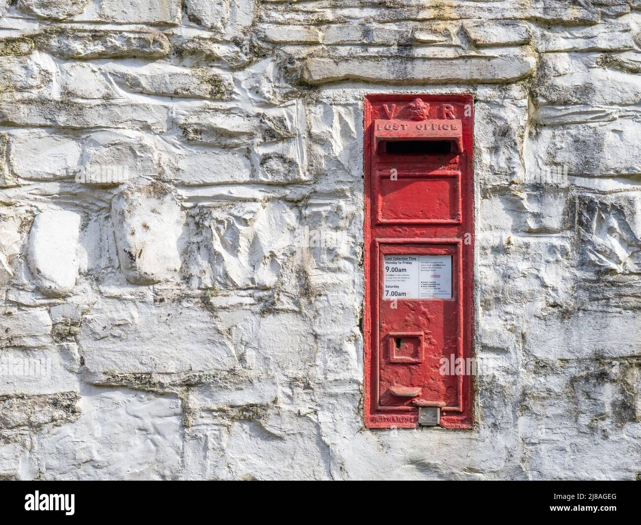 NORTH DEVON, MÄRZ 13 2022: Leuchtend rote viktorianische Post-Briefkasten in alter Wand. Devon, Großbritannien. Stockfoto