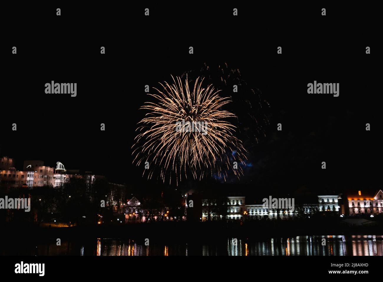 Feuerwerk über der gewöhnlichen europäischen Stadt in der Nacht in der Nähe von Wasser, orange Stockfoto