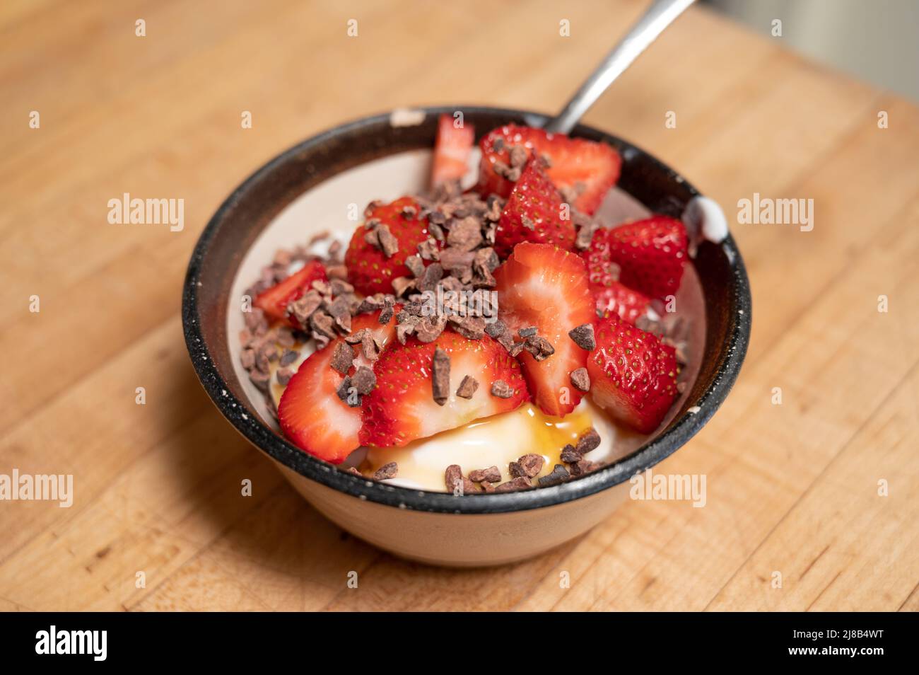 Erdbeeren in einer kleinen Schüssel auf Joghurt und garniert mit Kakaonibs Stockfoto