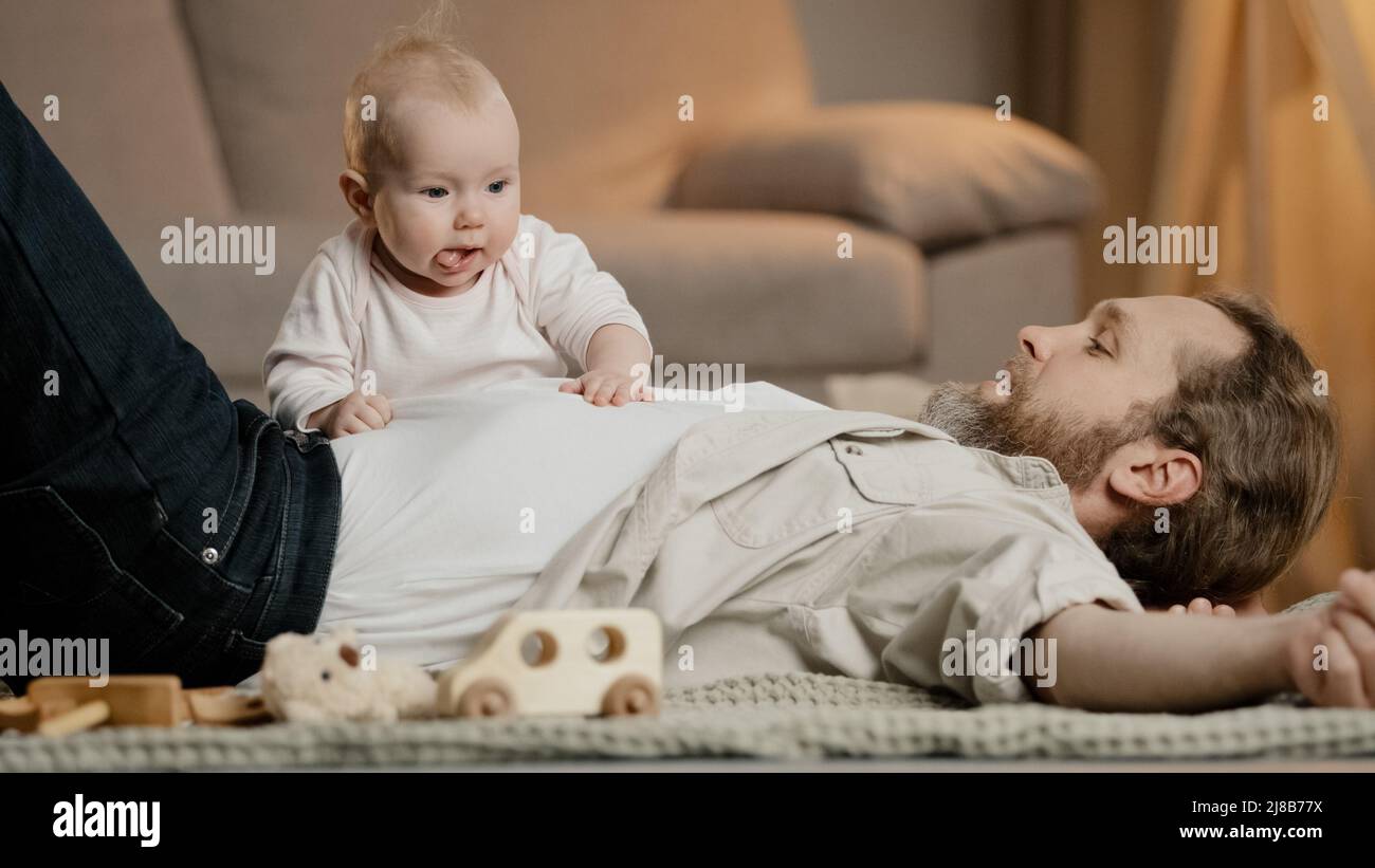 Kaukasischer Familienvater mit kleiner Tochter Sohn liegen auf dem Boden zu Hause spielen. Baby girl junge neugeborenes Kind kriecht über Vater Kinderbetreuung Vaterschaft Stockfoto