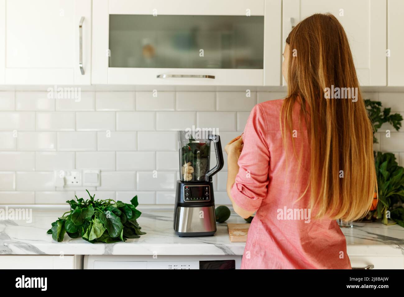 Frau bereitet leckeren grünen Smoothie in der Küche, Blick von hinten Stockfoto