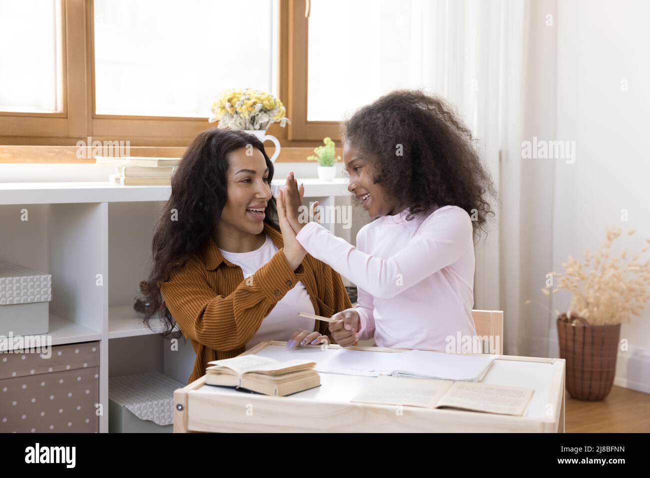 Afrikanische Mutter lobte die kleine Tochter für den erfolgreichen Abschluss der Schularbeit Stockfoto