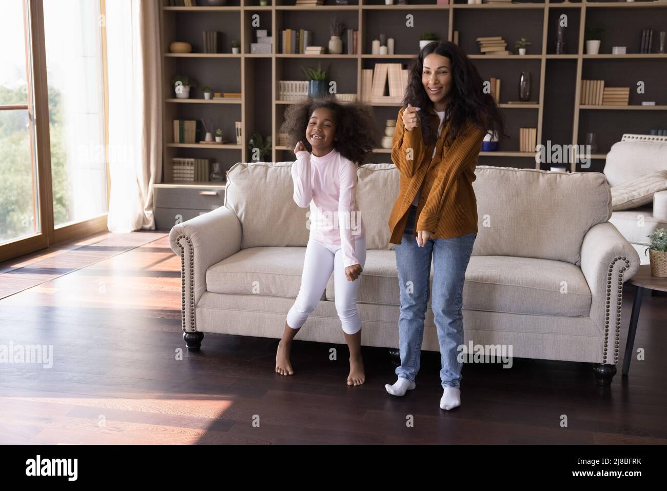 Fröhliche afrikanische Mädchen und Mutter tanzen im modernen Wohnzimmer Stockfoto