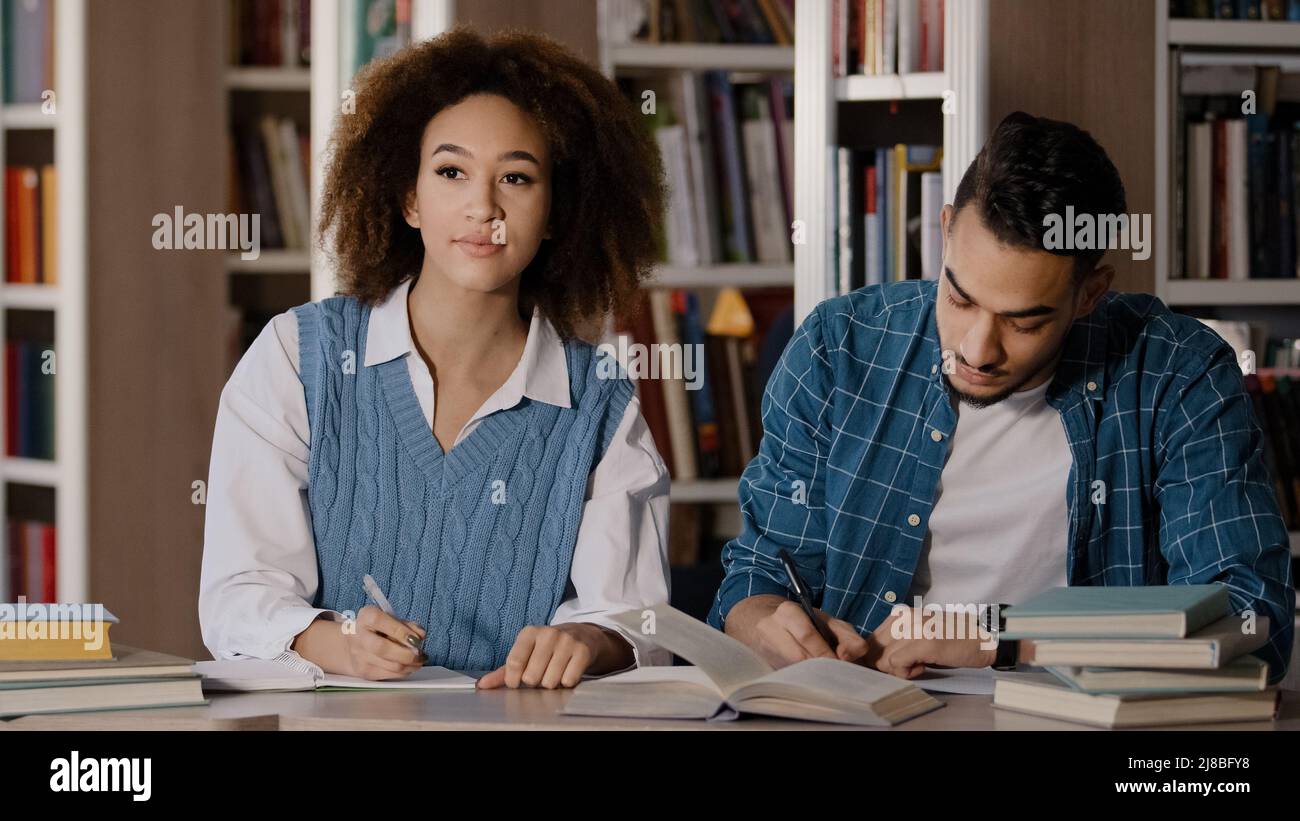 Zwei Studenten, junger Mann und Mädchen, die Hausaufgaben machen, sitzen am Schreibtisch in der Bibliothek und schreiben Notizen aufmerksam dem Dozenten beim Unterricht in der Klassenzimmer-Gruppe zu hören Stockfoto