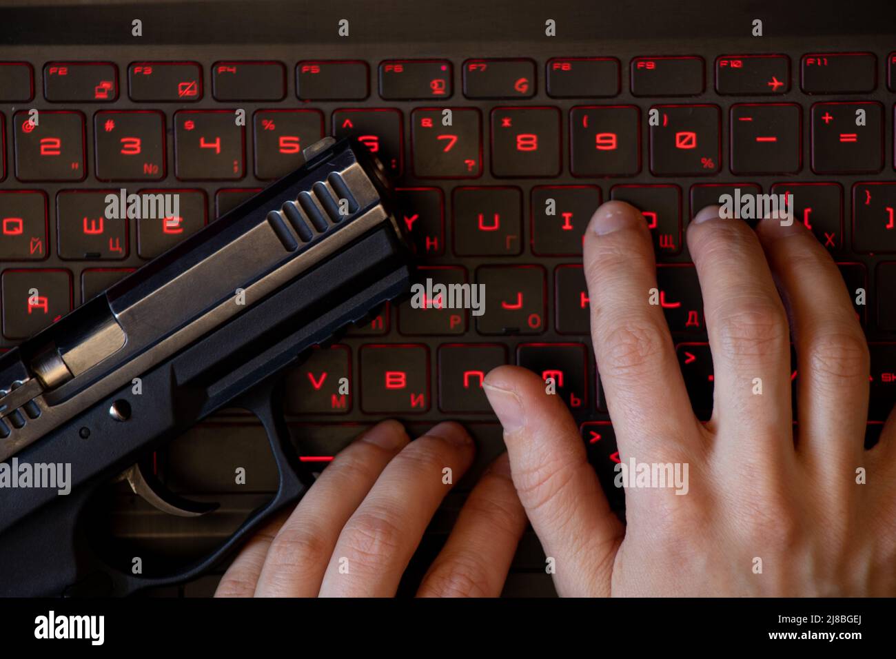 Eine Waffe liegt auf einer schwarzen Laptop-Tastatur mit roter Hintergrundbeleuchtung und einer Frauenhand auf der Tastatur, Sicherheitsbedrohung, Cyber-Angriff, System-Hacking, Arbeit Stockfoto