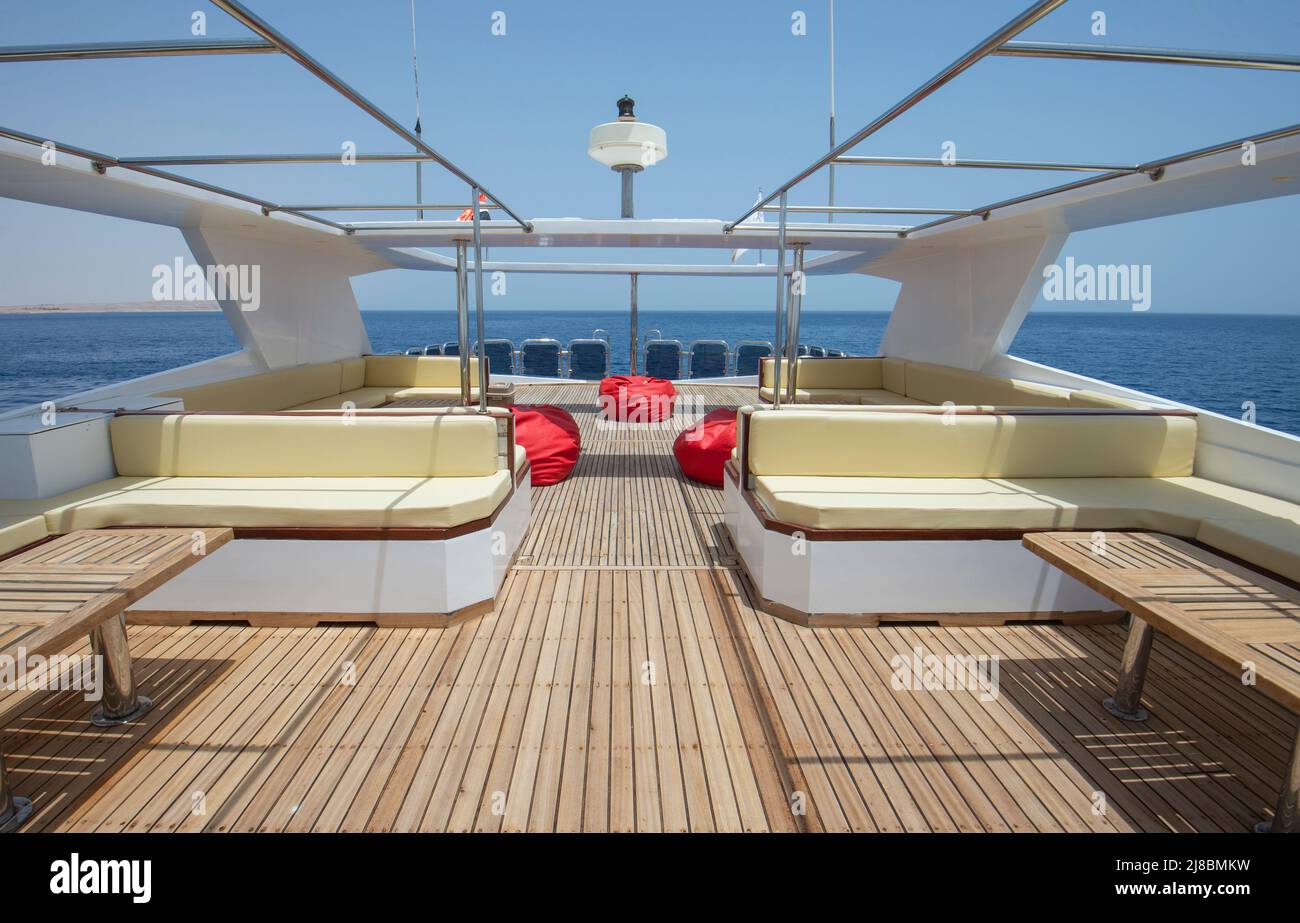 Sonnendeck aus Teakholz einer großen Luxus-Motoryacht mit Stühlen, Sofa-Tisch und tropischem Meerblick im Hintergrund Stockfoto