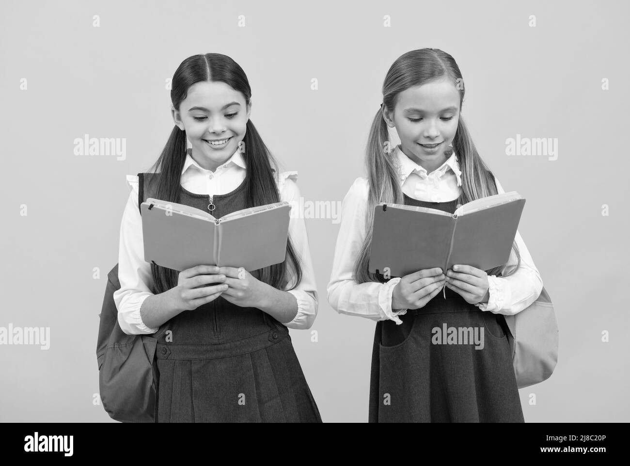 Kleine Kinder in Schuluniformen lesen Bibliotheksbücher gelben Hintergrund, lesen Stockfoto