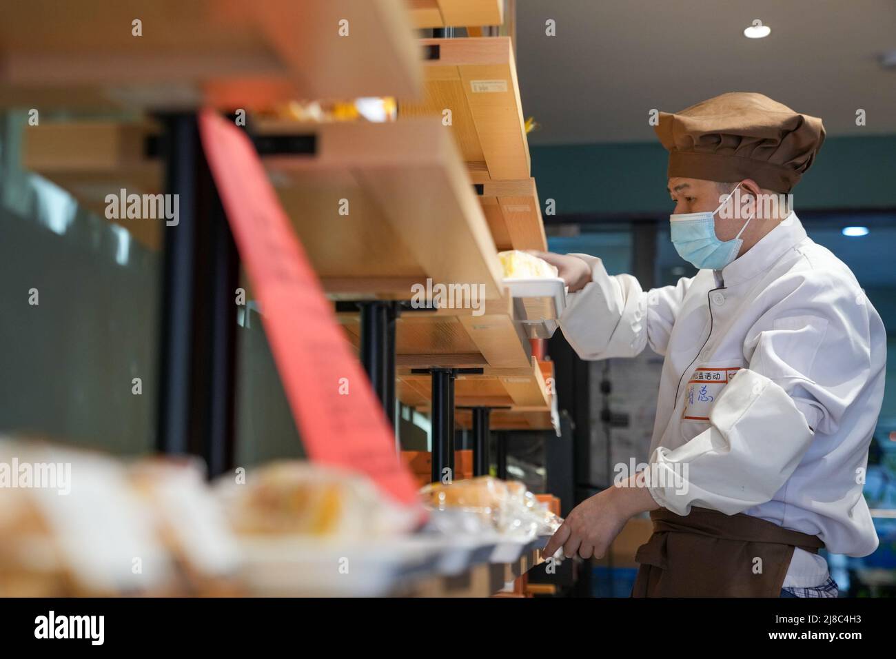 (220515) -- NANJING, 15. Mai 2022 (Xinhua) -- Ein geistig behinderter Mitarbeiter arrangiert Brot in der Bäckerei Amity in Nanjing, der ostchinesischen Provinz Jiangsu, 10. Mai 2022. Die Bäckerei wurde 2007 gegründet und bietet in den letzten 15 Jahren fast 100 geistig behinderten Menschen berufliche Ausbildungs- und Beschäftigungsmöglichkeiten. (Xinhua/Li Bo) Stockfoto