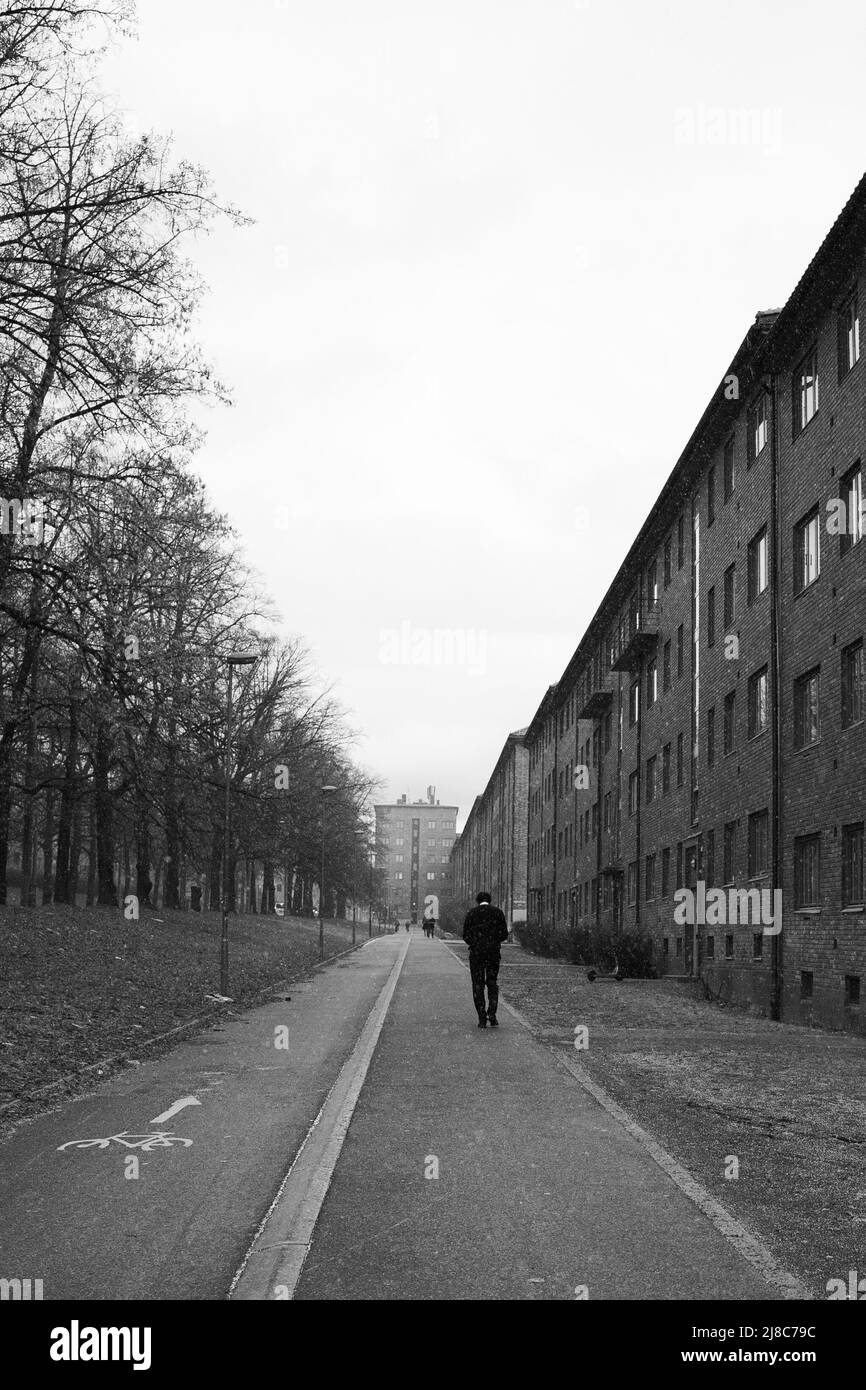Ein Mann, der auf einer langen Straße mit Bäumen und Gebäuden läuft Stockfoto