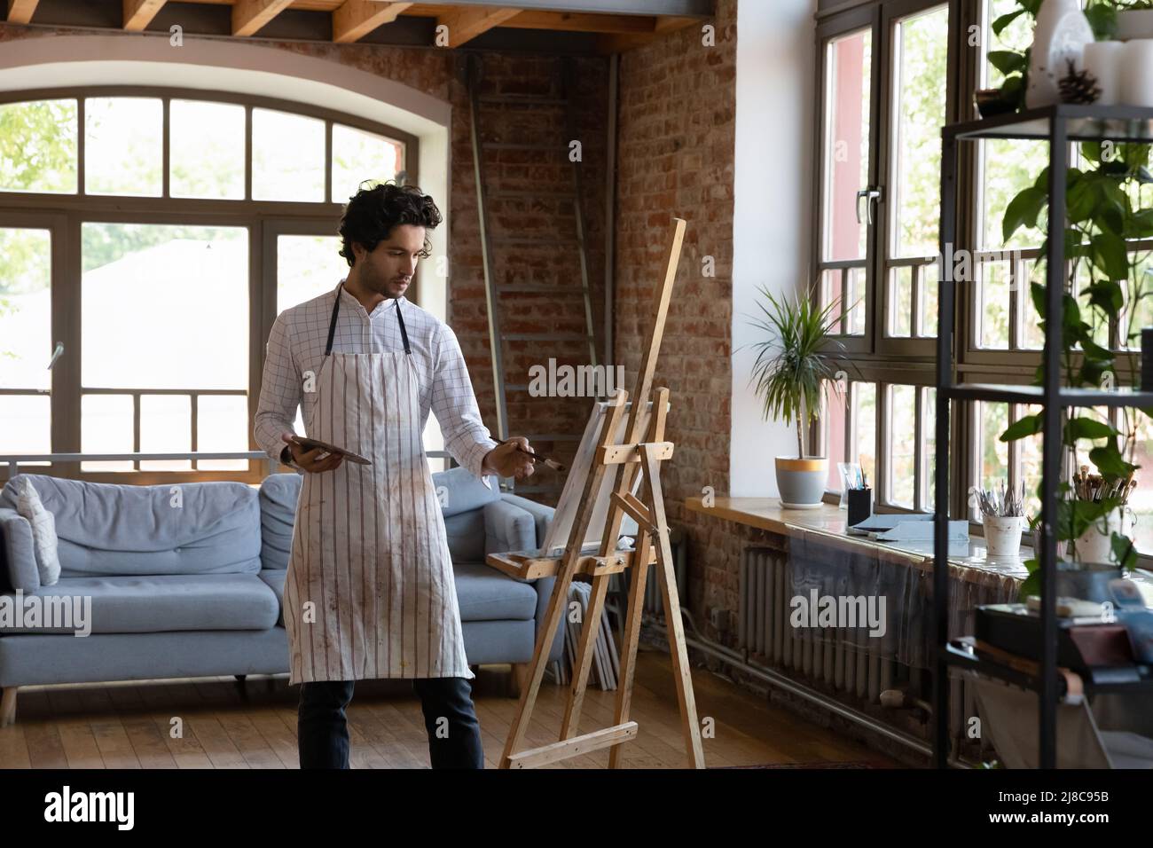 Millennial Mann Maler hält Palettenmalerei auf Leinwand in der Werkstatt Stockfoto