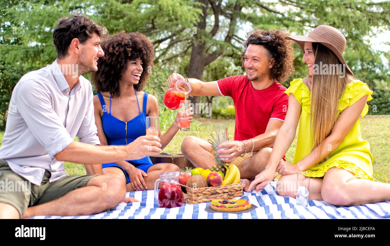 Sommerferien Picknick im Freien. Multirassische Gruppe von Freunden mit Essen und Getränken auf einer Decke in einem Park Garten. Menschen süße Pause genießen Stockfoto