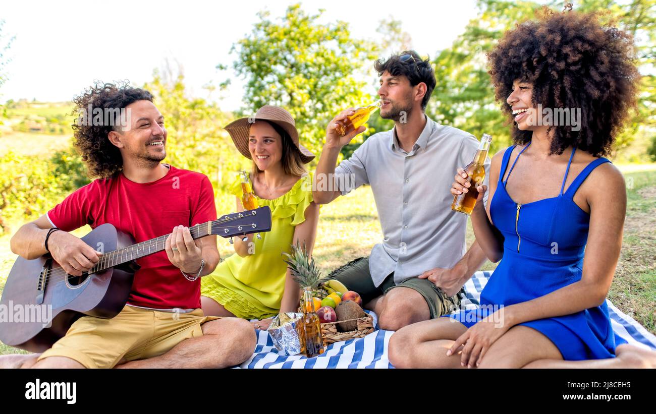 Sommerferien Picknick im Freien. Multirassische Gruppe von Freunden, die Essen und Bier trinken, die auf einer Decke in einem Parkgarten liegen. Menschen Happy Hour en Stockfoto
