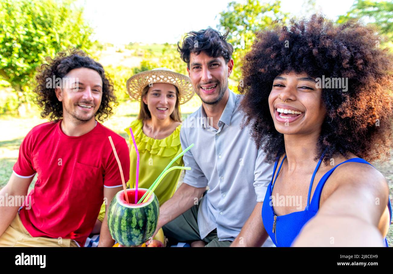 Sommerferien Picknick im Freien. Multirassische Gruppe von Freunden, die aus Wassermelone trinken, die auf einer Decke in einem Parkgarten liegt Stockfoto