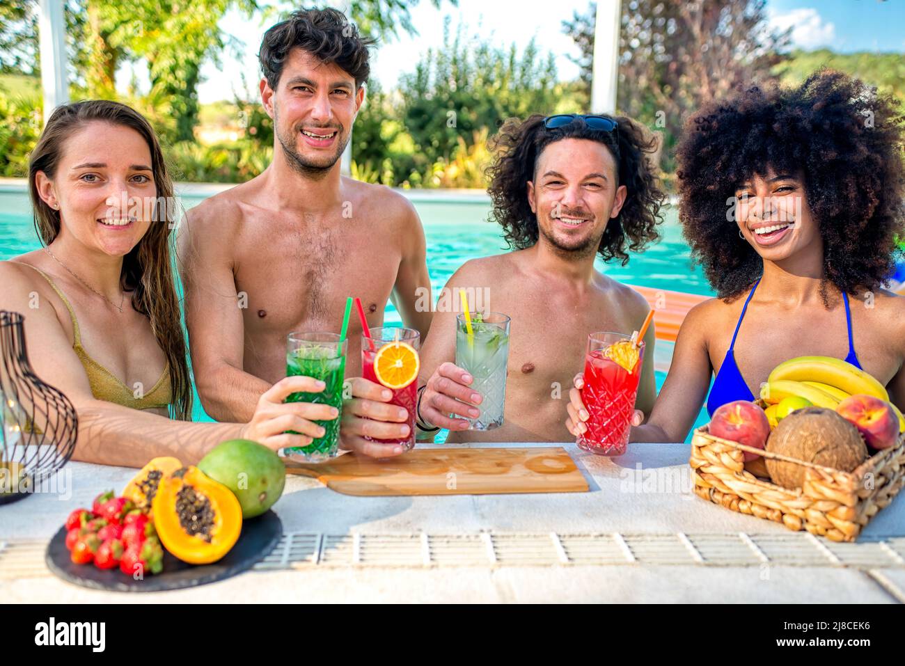 Sommerschwimmbad-Party! Glückliche multirassische Gruppe von Freunden, die im Wasser stehen, mit Getränken, die heiße Feiertage im Freien feiern Stockfoto