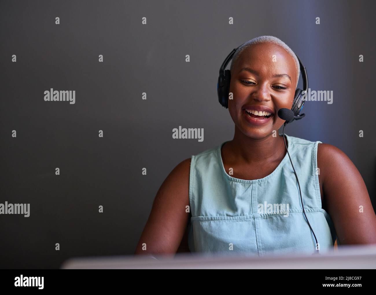 Ein junger Agent des schwarzen Callcenters lacht während eines Anrufs mit einem Headset Stockfoto