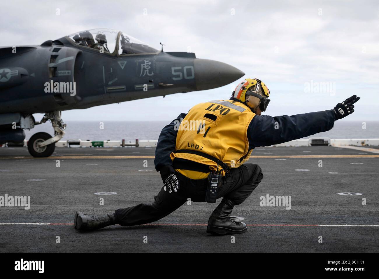 Die US-Marine Aviation Bootswerber Mate 1. Klasse Reymond Rallos signalisiert einem Marine Corps AV-8B Harrier, der an die Marine Expeditionary Unit 22. angeschlossen ist, vom Flugdeck des amphibischen Sturmschiffs USS Kearsarge der Wasp-Klasse am 20. April 2022 auf den Atlantischen Ozean zu starten. Stockfoto