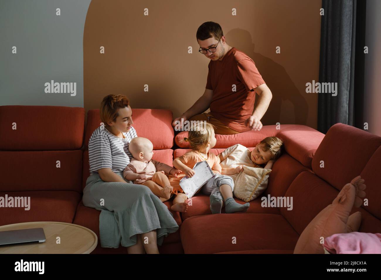 Große Familie auf der Couch zu Hause. Eltern mit Kindern auf dem Sofa während eines sonnigen Tages verbringen Freizeit. Mutter und Vater mit drei Kindern, die Buch lesen. Modern Stockfoto