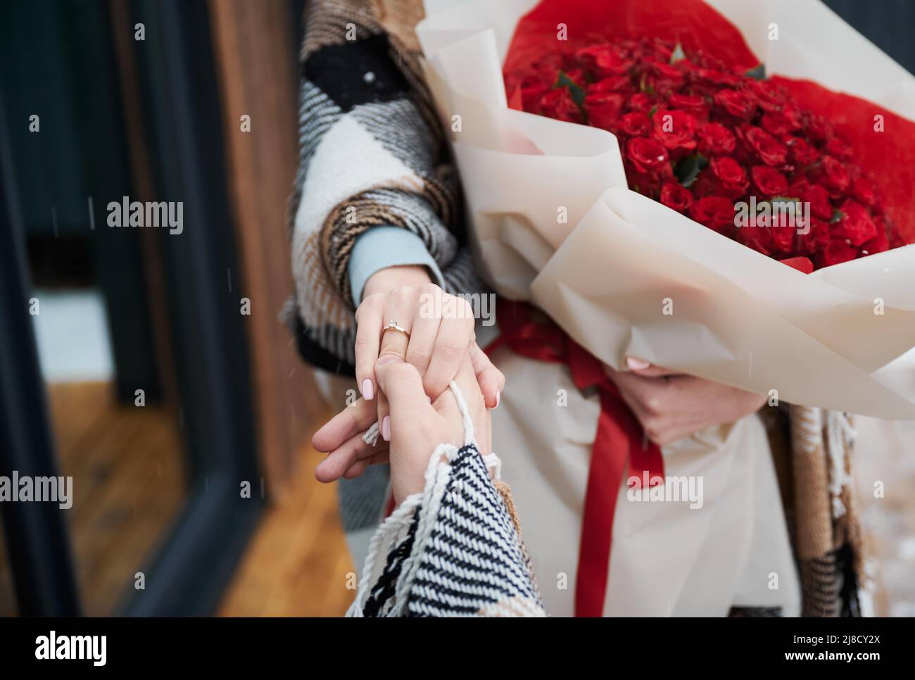 Nahaufnahme der verlosten Paarhände mit Verlobungsring am weiblichen Finger. Mann in der Liebe hält Verlobte Hand, während Frau Strauß Rosen hält. Konzept von Liebe, Romantik und Ehe. Stockfoto