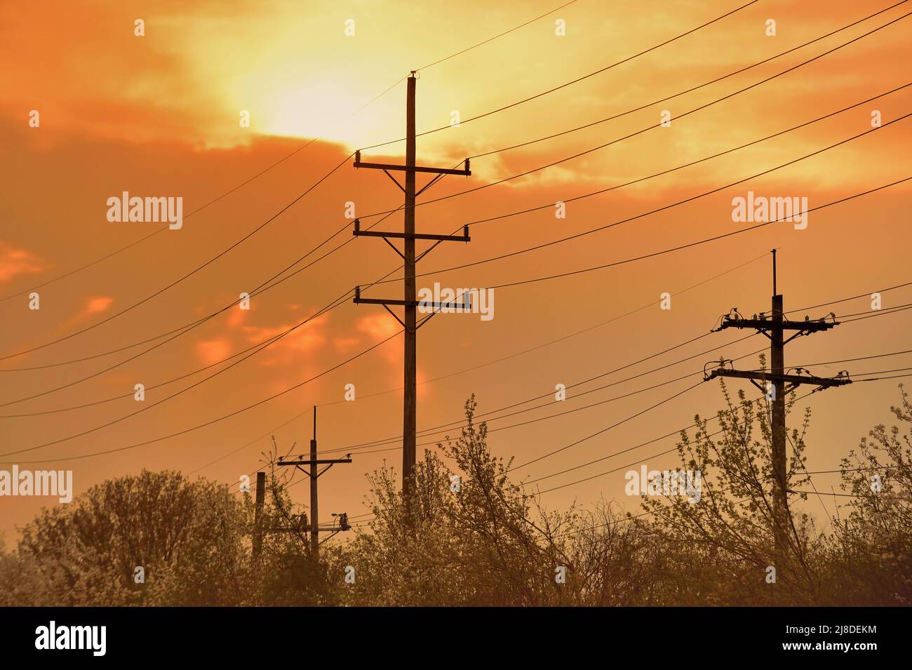 Genf, Illinois, USA. Telefonmasten und Telefonleitungen stehen kurz vor Sonnenuntergang an einem Frühlingsabend in den Wolken vor einem Farbdisplay. Stockfoto