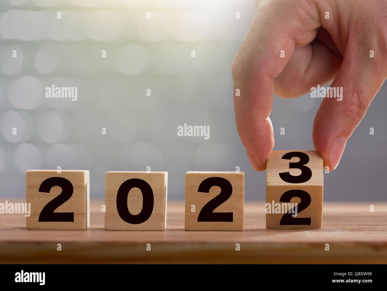 Der Mann dreht den Block 3 mit den Fingern. Holzblöcke mit 2022 - 2023 Nummer auf dem Tisch. 2023 Neujahrs-Konzept Stockfoto