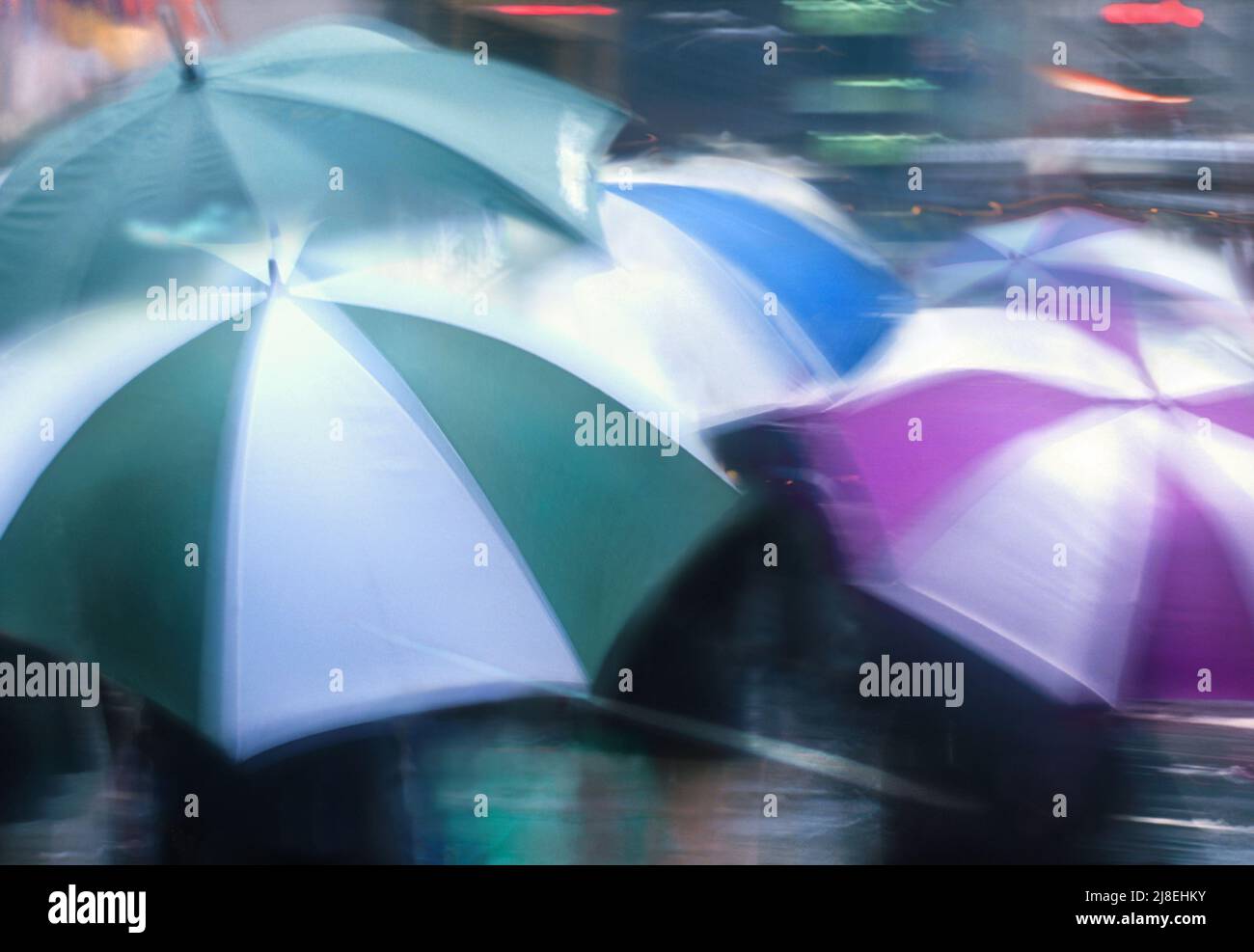 An einem regnerischen Tag können Sie bunte Regenschirme aus der Nähe öffnen. Straßenszene. Nasser Bürgersteig und vorbeifahrende Straße. Nicht erkennbare Menschen Stockfoto