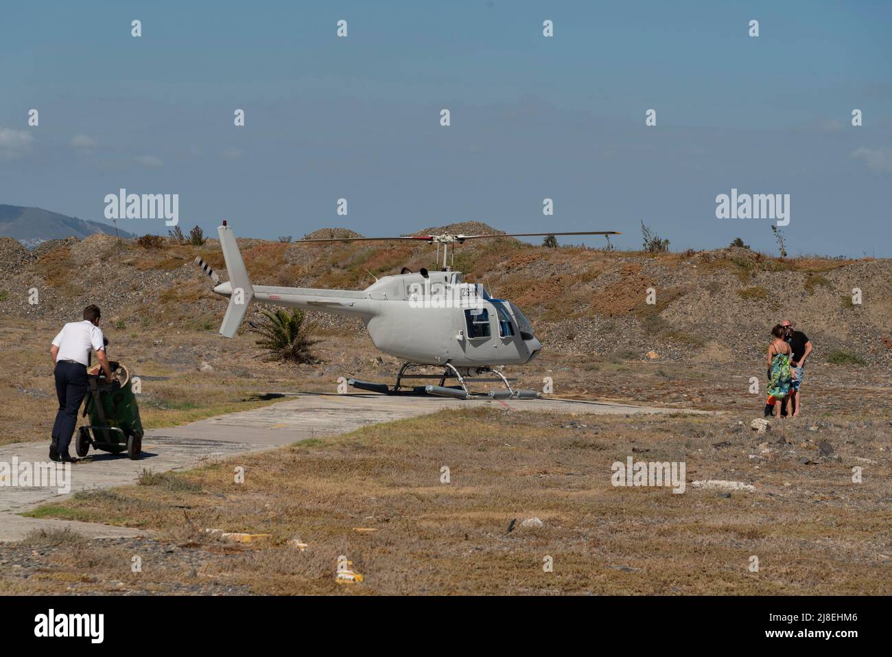 Kapstadt, Südafrika. 2022. Statischer Hubschrauber und Besatzungsmitglied, das Barrel Avgas-Flugkraftstoff schiebt, um das Aicraft aufzutanken. Passagiere warten auf b Stockfoto