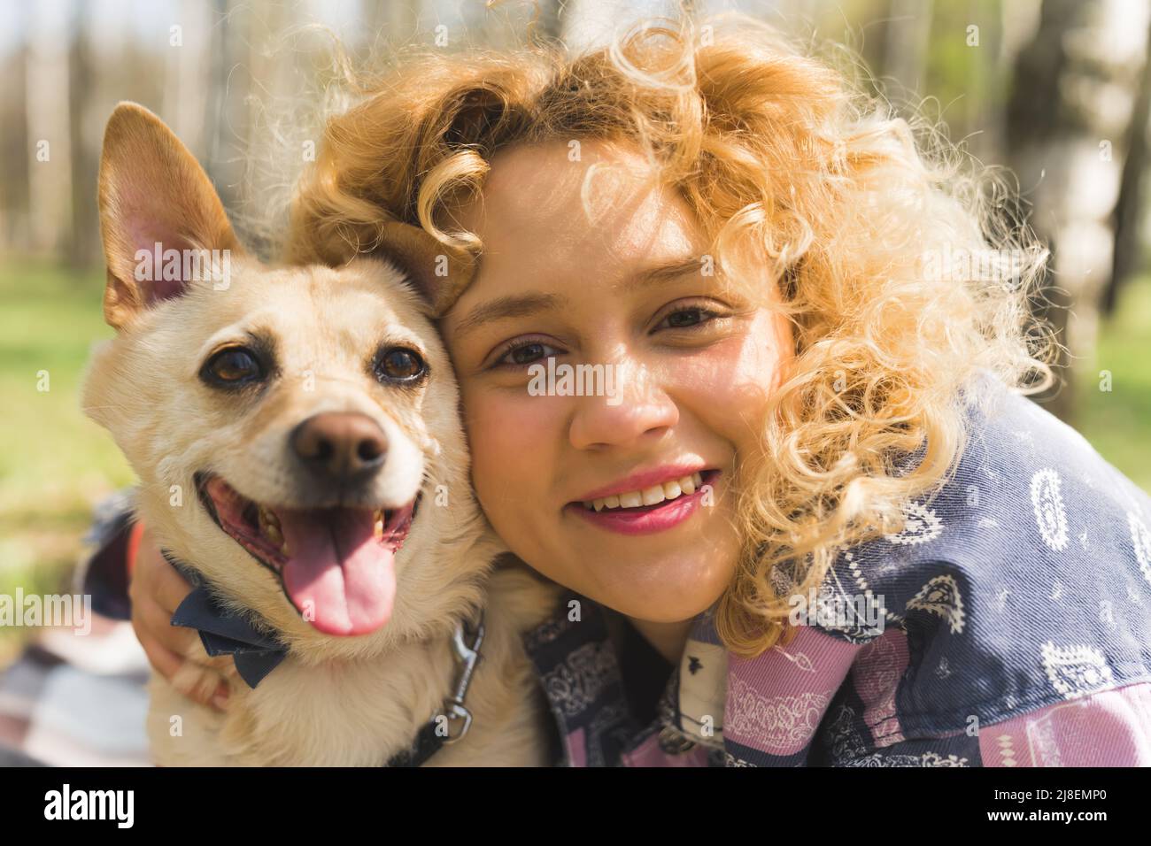 Im Freien Nahaufnahme Porträt einer fröhlichen schönen natürlichen kaukasischen Frau mit lockigen blonden Haaren und einem gemischten Rasse glücklichen Hund. Hochwertige Fotos Stockfoto