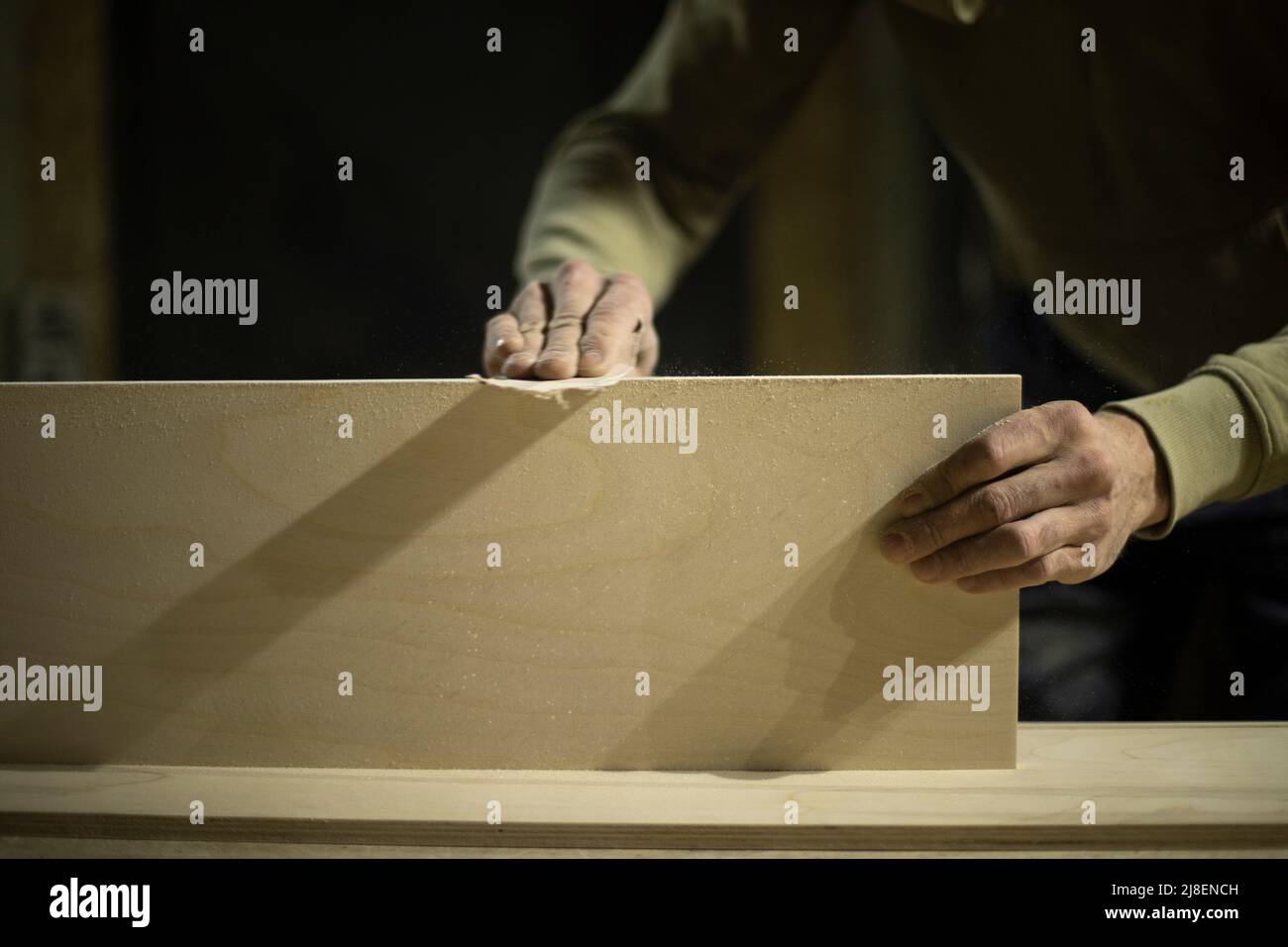 Der Zimmermann schleift das Brett. Der Mensch schafft Möbel. Hände halten Schleifpapier. Arbeiter verarbeitet Holz. Stockfoto