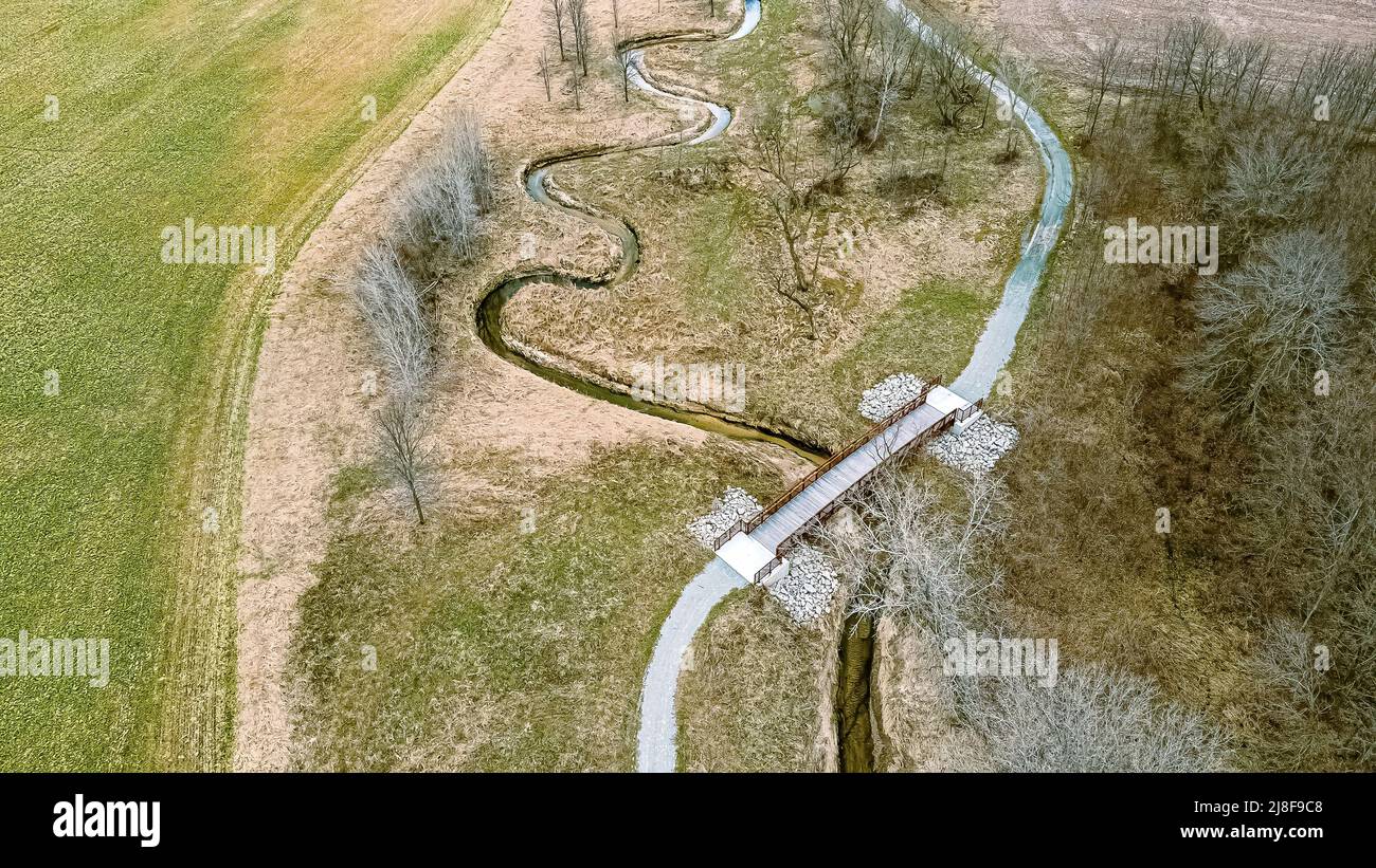 Ein spiralförmiges Flussbett folgt im Frühjahr einer Spur, nachdem der Schnee geschmolzen ist. Eine Brücke erstreckt sich über den Bach. Stockfoto