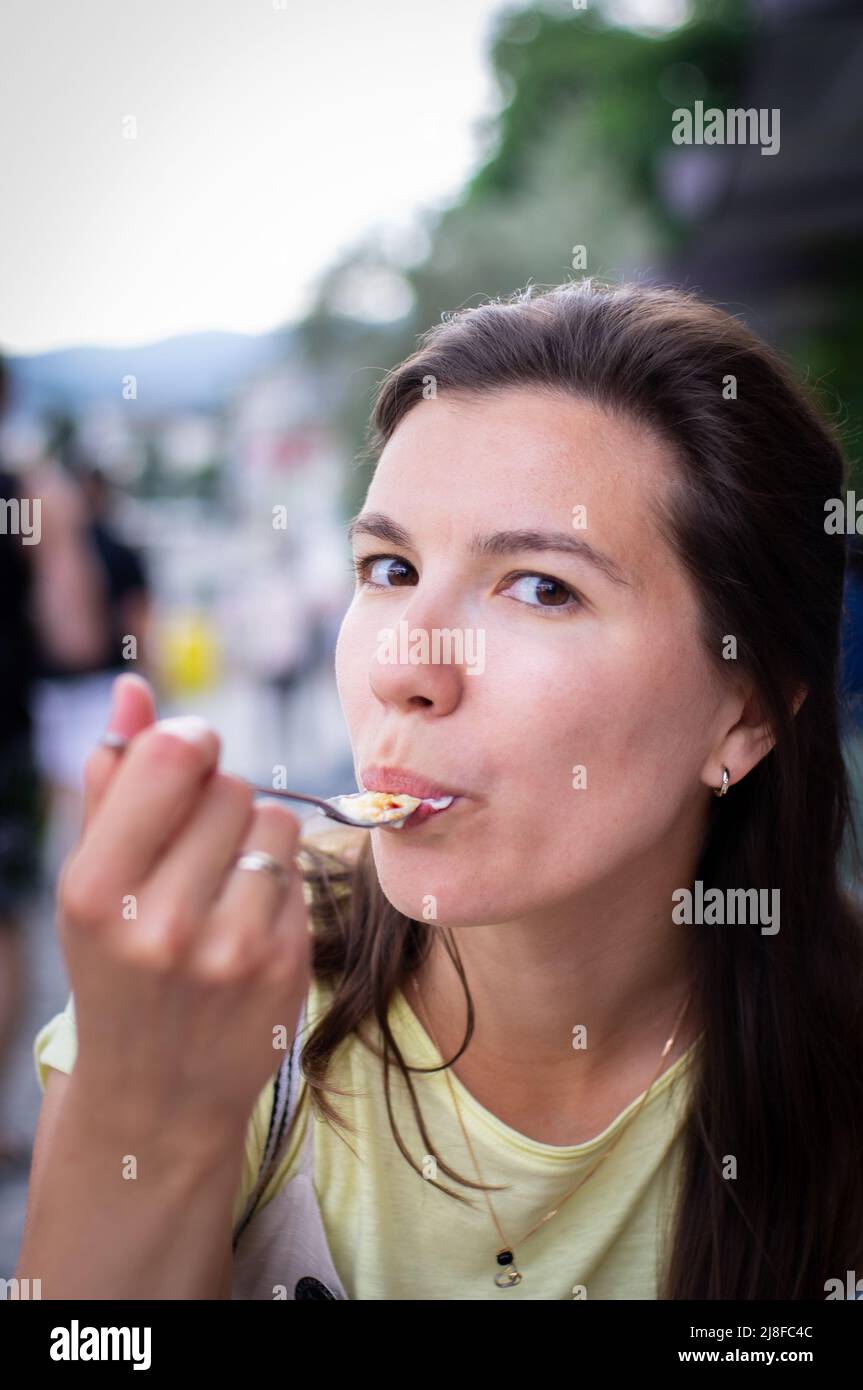 Eine junge Frau, die draußen in einem Restaurant Creme Brulee isst, ein Konzept von Urlaub und Sommer genießen. Vertikales Foto. Stockfoto