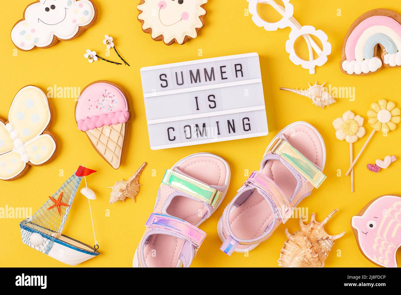 Der Sommer kommt. Motivationszitat auf Leuchtkasten und niedlichen Sommer-Symbolen auf gelbem Hintergrund. Draufsicht, Flat Lay. Kreative inspirierende Sommerkonz Stockfoto