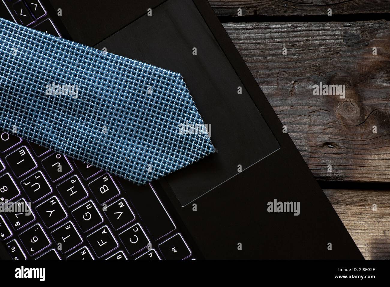Eine blaue Krawatte liegt auf einem schwarzen Laptop auf einem Holztisch zu Hause, arbeiten Sie online Stockfoto