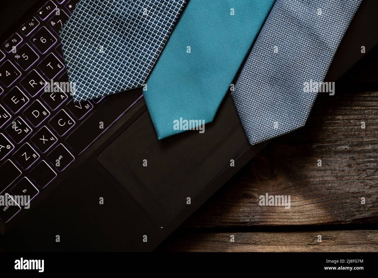 Drei blaue Krawatten liegen auf einem schwarzen Laptop auf einem Holztisch zu Hause, arbeiten online Stockfoto