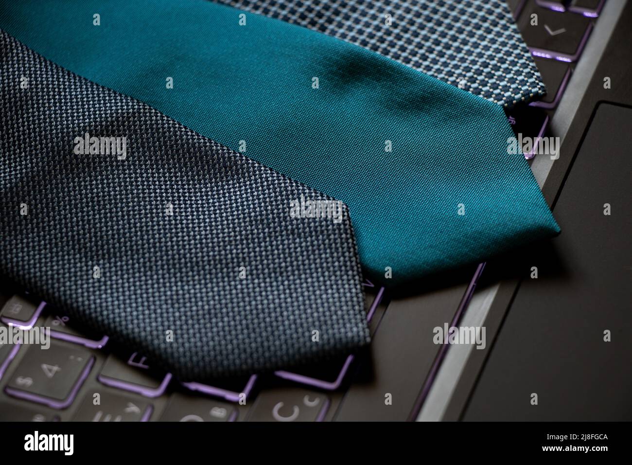 Drei blaue Krawatten liegen auf einem schwarzen Laptop auf dem Schreibtisch zu Hause und arbeiten online Stockfoto
