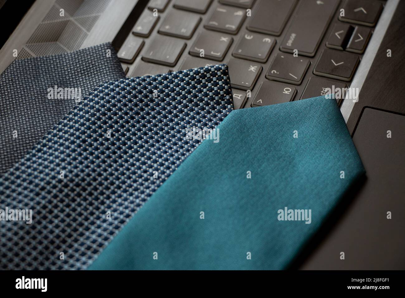 Drei blaue Krawatten liegen auf einem schwarzen Laptop auf dem Schreibtisch zu Hause und arbeiten online Stockfoto