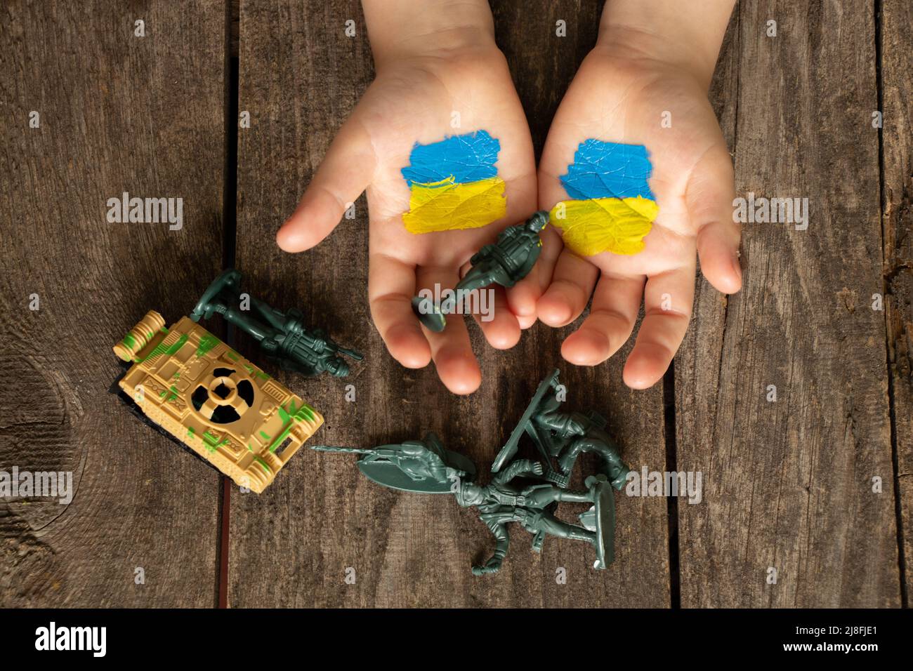 Auf die Hände eines Kindes wird eine gelb-blaue Flagge der Ukraine gezeichnet, Soldaten und ein Panzer liegen nebeneinander, Krieg in der Ukraine mit Russland, Frieden in der Ukraine Stockfoto