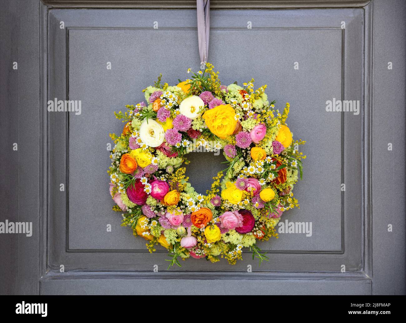 Blumenkranz hängt an einer Holztür des Hauses. Frische Wildblumen und Kräuter, Dekoration, Vorderansicht. Sonniger Frühlingstag. Frauen oder Mütter Tag-Frau Stockfoto