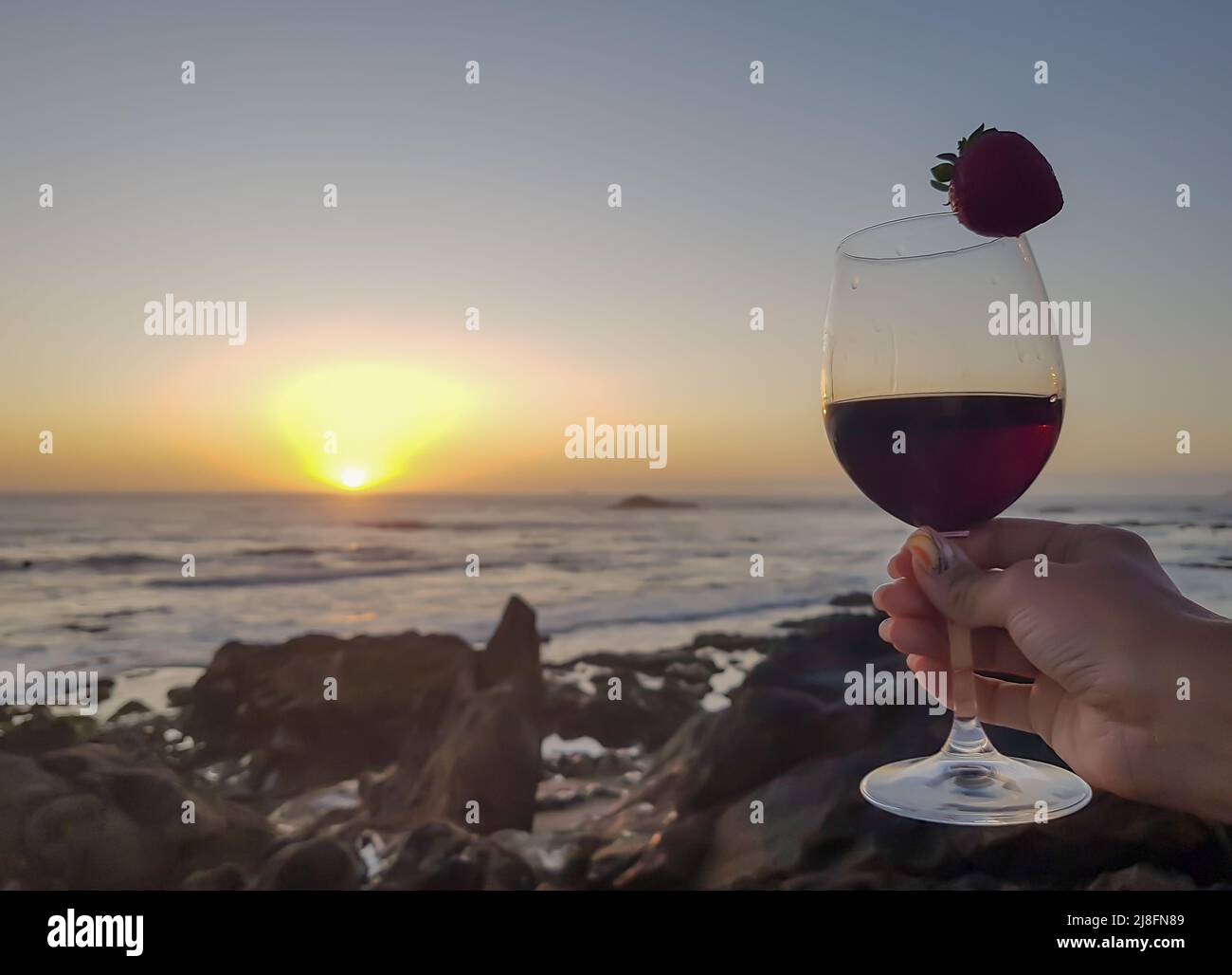 Frau mit einem Glas Rotwein und Erdbeere am Strand. Sonnenuntergang wunderbare Zeit Stockfoto