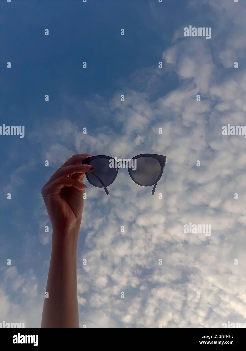 Frau Hand mit Sonnenbrille auf dem Hintergrund des blauen Himmels. Blick auf den Himmel durch Sonnenbrille Stockfoto